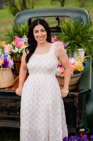 A pink bow dress on a while fabric. Smocked top and empire waist give a flattering look while the extra details like ruffles straps make it extra beautiful.