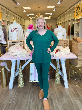 Woman in a green outfit standing in a store with mannequins and clothing displays.