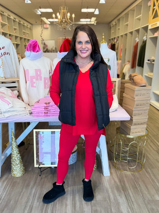 Woman in a red outfit with a black vest standing in a store setting.