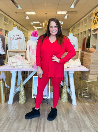 Woman in a red outfit standing in a store with mannequins and clothing in the background.