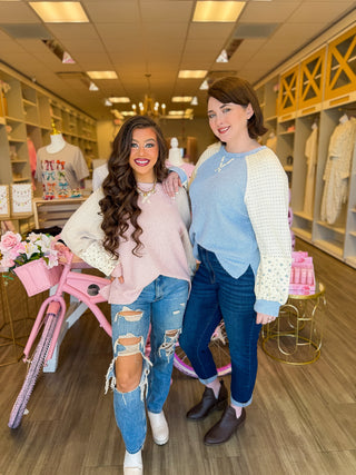 Pink and blue color block sweaters with floral sleeves modeled inside Bailey Kate Boutique. Cozy fall fashion with feminine, pastel details.