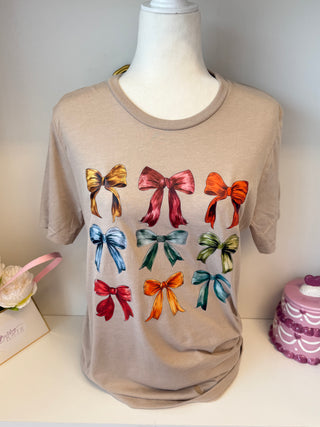 Beige graphic t-shirt with colorful illustrated bows in red, blue, green, and orange – playful boutique bow tee.